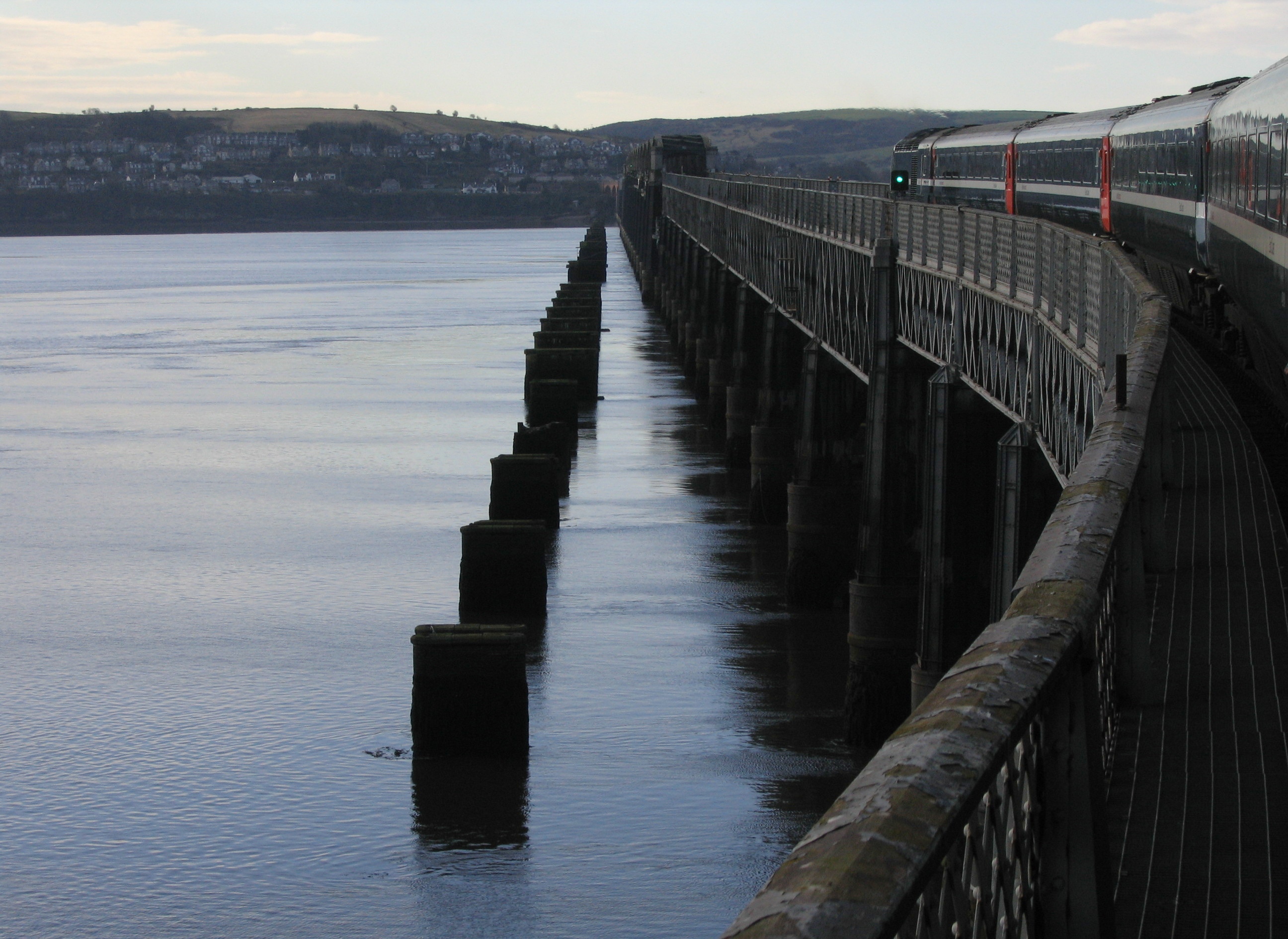 Tay Railway Bridge seen alongside a passing train, with the piers of the earlier bridge standing in the estuary