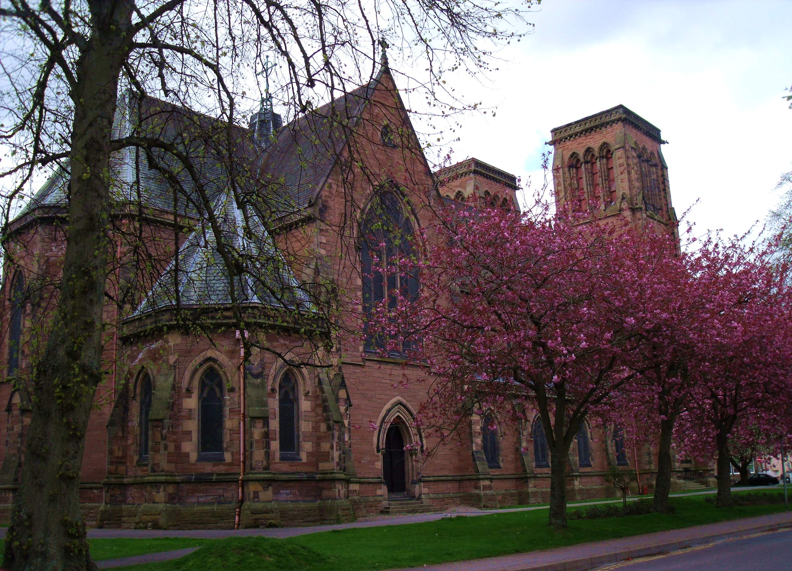 Red sandstone Gothic Revival Inverness Cathedral seen through flowering trees from Bishop’s Road
