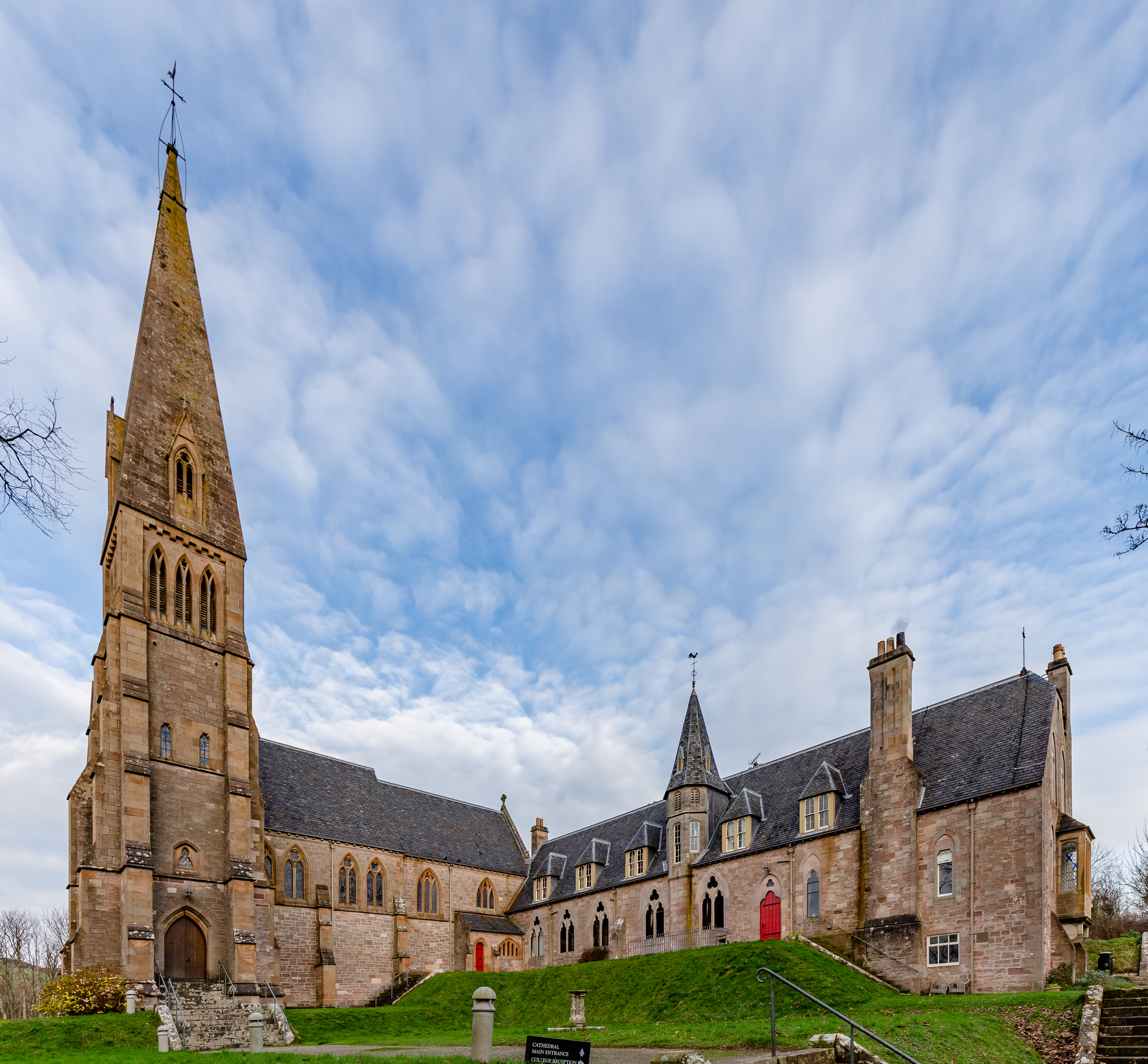 Cathedral of the Isles with its tall stone spire, pointed windows and adjoining collegiate range on a grassy slope.