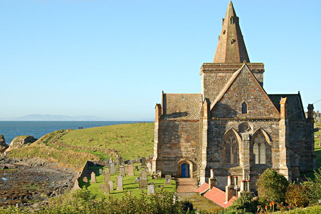 St Monans Church standing beside the rocky shore, with its crossing tower and spire against the sea.